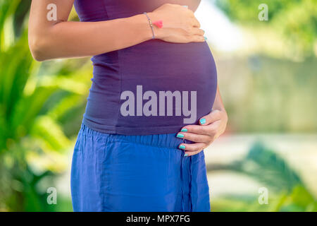 Photo Gros plan d'un ventre de femme enceinte debout dans le parc, avec douceur et amour future mère de toucher son ventre, nouveau concept de vie Banque D'Images