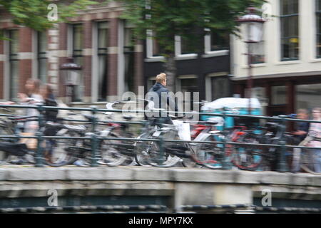 Un homme chevauche son vélo à travers un canal à Amsterdam, aux Pays-Bas. Banque D'Images