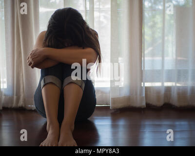 Triste et désespéré femme embrasser son genou et pleurer alors qu'il était assis seul sur le plancher. Banque D'Images