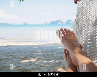 Pieds femme Gros plan allongé sur un hamac avec des arbres et une vue magnifique sur la mer / plage vue arrière-plan. Banque D'Images