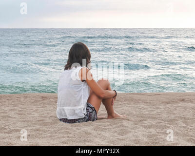 Femme à la recherche en mer tout en vous relaxant sur le sable contre le ciel au coucher du soleil Banque D'Images