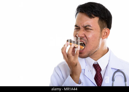 Studio shot of young Asian man eating donut médecin avec les yeux clo Banque D'Images