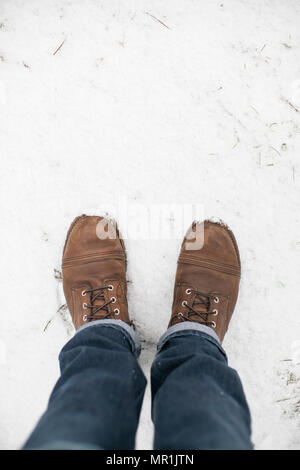 Pieds d'un homme portant des bottes de travail de l'aile rouge et bleu jeans debout dans la neige. Banque D'Images