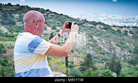 Homme d'âge moyen vue latérale rapprochée, prendre une photo du paysage sur une colline en regardant vers la ville lointaine, Kyrenia, nord de Cypress, Banque D'Images