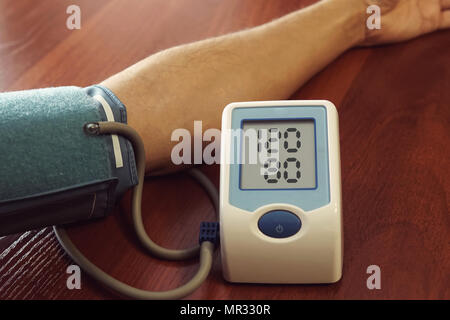 La mesure de la pression artérielle du patient. men's main avec un appareil pour mesurer la pression sur l'arrière-plan d'une table en bois. La tension artérielle normale. En bonne santé Banque D'Images
