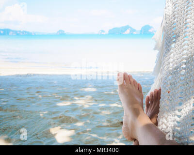 Pieds femme Gros plan allongé sur un hamac avec des arbres et une vue magnifique sur la mer / plage vue arrière-plan. Banque D'Images