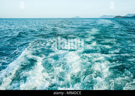 Tracé des courbes avec mousse blanche sur l'eau de mer de surface derrière fast moving bateau ou yacht. Les petites îles dans la brume sèche sur l'horizon. Ciel bleu avant le coucher du soleil. Banque D'Images