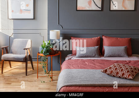 Chambre d'hôtel confortable intérieur avec un lit double avec oreillers à côté d'une table de chevet, un fauteuil et des plantes Banque D'Images