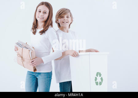 Girl holding vieux papiers et le garçon l'exécution d'une poubelle qui pose pour une photo sur un fond blanc Banque D'Images