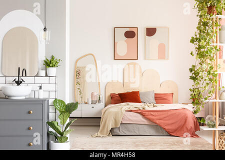 Oreillers orange sur le lit à côté d'un miroir à l'intérieur chambre à coucher moderne avec des affiches et une salle de bains privative. Photo réelle Banque D'Images