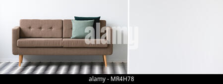 Brown table avec deux coussins vert debout dans un espace ouvert de l'intérieur blanc avec sol en damier Banque D'Images