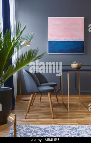 Photo réelle de l'intérieur salle à manger avec deux chaises, debout devant une table, sur un sol en bois avec tapis à motifs, à côté d'un mur avec une peinture d'un Banque D'Images