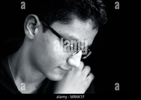 Portrait d'un jeune adolescent posant avec un petit sourire sur son visage dans un fond sombre portant des T-Shirt à capuchon vert.Low key portrait. Banque D'Images