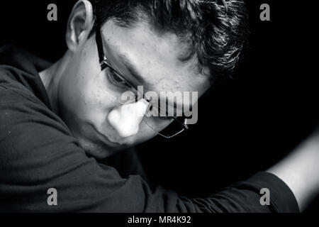 Portrait d'un jeune adolescent posant avec un petit sourire sur son visage dans un fond sombre portant des T-Shirt à capuchon vert.Low key portrait. Banque D'Images
