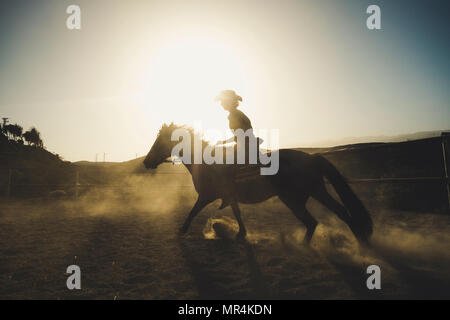 Belle fille monter un cheval en silhouette et rétroéclairage avec sunflare et la poussière de la terre. epic et héros de droit pour la vitesse et la vie cowbot et ad Banque D'Images