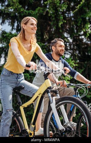 Young smiling couple riding bicycles together in park Banque D'Images