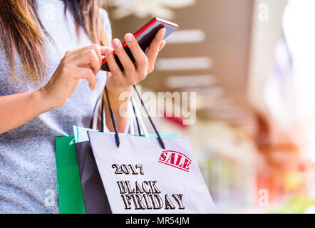 Woman holding shopping bags faire les achats en ligne sur son téléphone portable dans le supermarché. Le vendredi noir vente concept. Banque D'Images