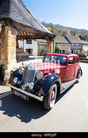 Un Red Rover 16 garé à côté de la croix du marché dans le sud du village des Cotswolds Wiltshire Castle Combe, UK Banque D'Images