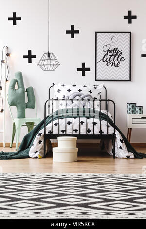 Tapis géométriques noir et blanc dans la chambre d'enfant avec jouet sur chaise à côté de lit avec oreillers gris Banque D'Images
