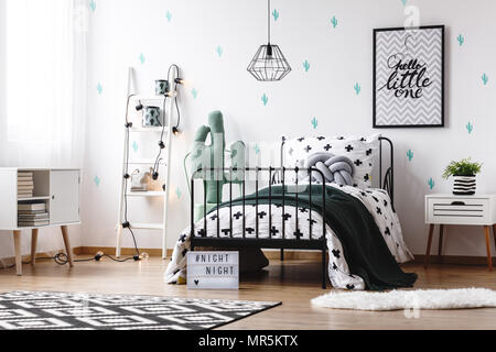 Jouet en forme de cactus à côté du lit avec couverture noire et tressé gris coussin dans chambre d'enfant avec la peinture Banque D'Images