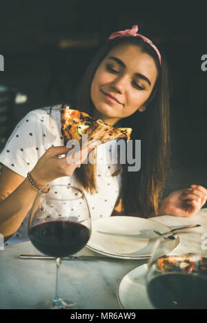 Young happy woman sitting at table eating pizza fraîchement cuits et de boire du vin rouge dans la cuisine italienne en plein air au café du soleil de l'été clair da Banque D'Images