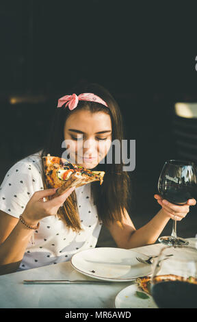 Young happy young woman sitting at table eating pizza et boire du vin rouge dans la cuisine italienne en plein air au café du soleil clair jour d'été, copy space Banque D'Images