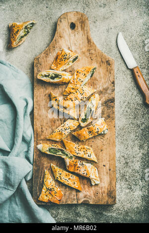 Télévision à jeter de Borek turc rouleau avec les épinards, le fromage feta, les graines de cumin noir coupé en tranches sur planche de bois sur fond de béton, vue du dessus. Tr Banque D'Images