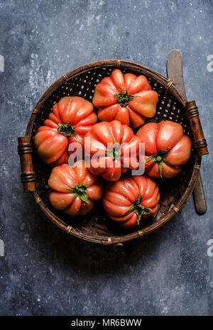 Tomates boeuf fraîchement cueillis dans un panier en osier sur un fond sombre. Banque D'Images