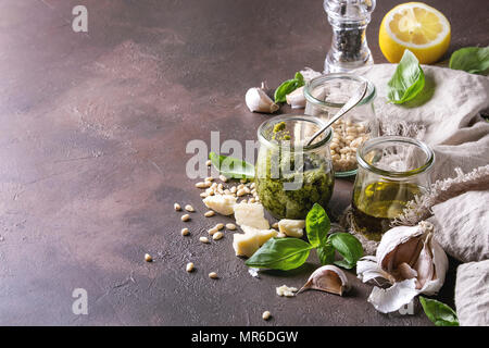 Sauce Pesto au basilic traditionnel dans un bocal en verre avec les ingrédients ci-dessus le basilic frais, l'huile d'olive, le parmesan, l'ail, les pignons de pin, citron sur tissu sur dark Banque D'Images