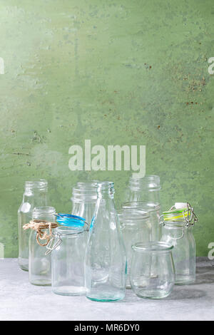 Variété de forme différente des bouteilles en verre vide ouvert avec et sans couvercle debout sur table avec mur gris vert comme arrière-plan. Banque D'Images