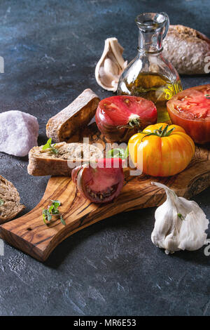 Variété de tomates biologiques rouge et jaune avec de l'huile d'olive, l'ail, le sel et le pain pour bruschetta salade ou sur la planche à découper en bois plus de texture bleu ba Banque D'Images