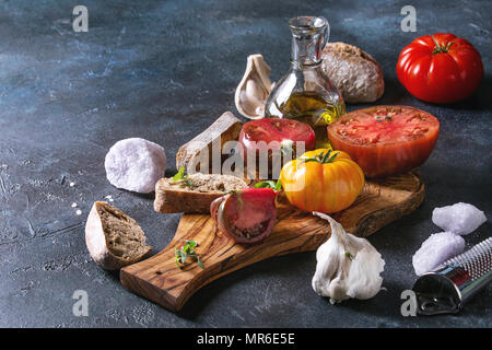 Variété de tomates biologiques rouge et jaune avec de l'huile d'olive, l'ail, le sel et le pain pour bruschetta salade ou sur la planche à découper en bois plus de texture bleu ba Banque D'Images