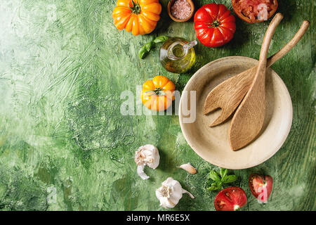 Variété de tomates biologiques rouge et jaune avec de l'huile d'olive, ail, sel, Bol en céramique vide, des cuillères en bois pour la salade verte sur fond de texture. À Banque D'Images