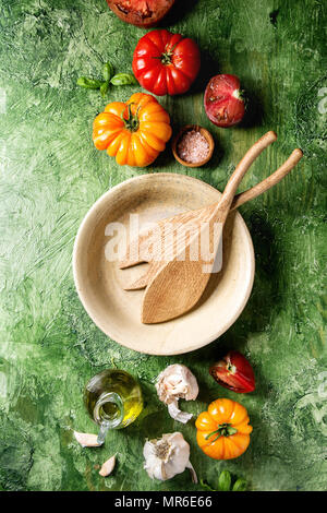 Variété de tomates biologiques rouge et jaune avec de l'huile d'olive, ail, sel, Bol en céramique vide, des cuillères en bois pour la salade verte sur fond de texture. À Banque D'Images