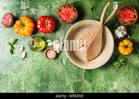 Variété de tomates biologiques rouge et jaune avec de l'huile d'olive, ail, sel, Bol en céramique vide, des cuillères en bois pour la salade verte sur fond de texture. À Banque D'Images