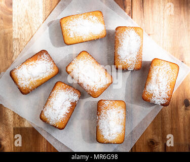 Petits gâteaux de pain orange saupoudrés de sucre glace sur du papier sulfurisé. Banque D'Images