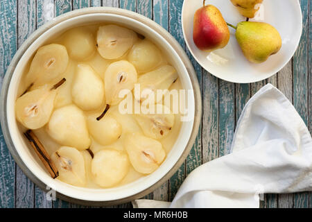 Un bol de confit de poires et un bâton de cannelle dans le sirop à côté de trois poires rouge non cuite. Banque D'Images