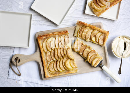 Une tarte coupée en morceaux sur un sol en bois servant de sélection, avec des plaques et un bol de crème. Banque D'Images