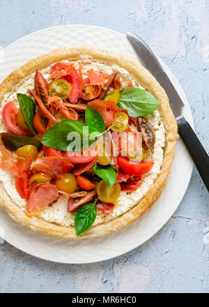 Tarte savoureuse ronde rempli de fromage feta, la pancetta, les tomates et les feuilles de basilic sur une plaque avec un couteau. Banque D'Images