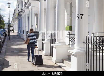 Une jeune femme passe devant le portique du stucco façades de maisons haut de gamme dans la région de Kensington, London, UK Banque D'Images