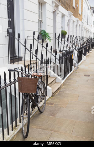 Un pushbike avec un panier en osier se penchant sur les balustrades victoriennes sur une rue chic smart de maisons mitoyennes en stuc à Chelsea, London, UK Banque D'Images