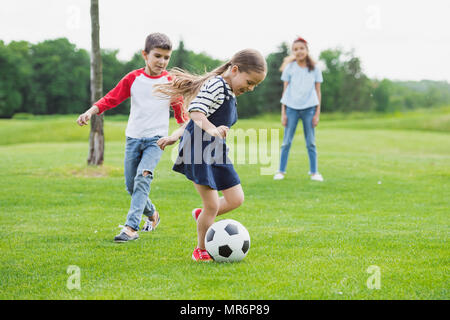 Adorable cheerful enfants jouant au foot avec ballon sur l'herbe verte Banque D'Images