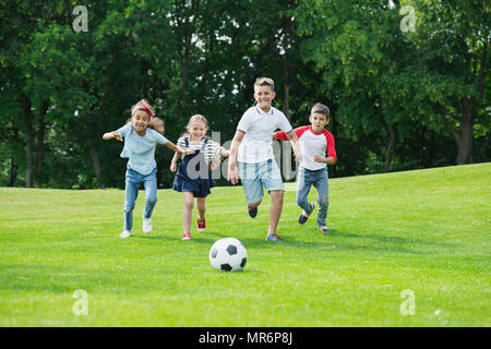 Happy Cute kids multiethnique à jouer au soccer avec ball in park Banque D'Images