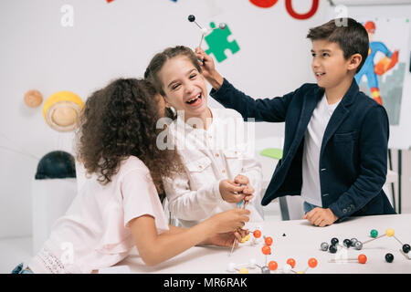 Travailler avec des écoliers multiethniques adorable modèle moléculaire et smiling in class Banque D'Images