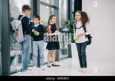 Groupe multiethnique d'élèves debout dans le couloir de l'école et déjeune Banque D'Images