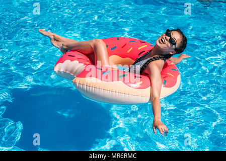 Young Asian woman flottant sur donut dans piscine gonflable Banque D'Images