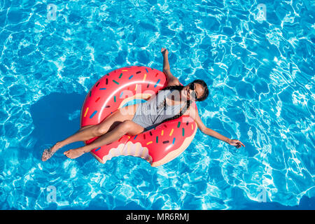 Young Asian woman flottant sur donut dans piscine gonflable Banque D'Images