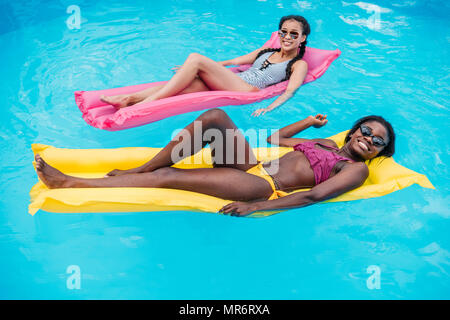 Les jeunes femmes multiethniques flottant sur le matelas gonflable dans la piscine du resort Banque D'Images