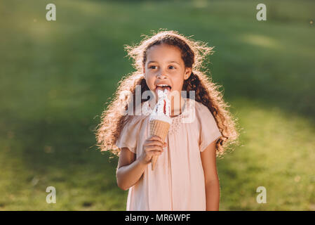 Adorable smiling african american girl licking ice cream cone dans la région de park Banque D'Images