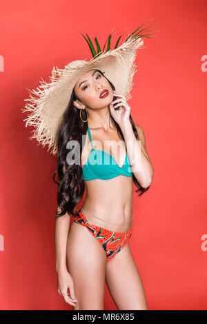 Demi-longueur de belle femme asiatique en maillot de bain et beach hat posant avec sa main toucher le menton et looking at camera Banque D'Images
